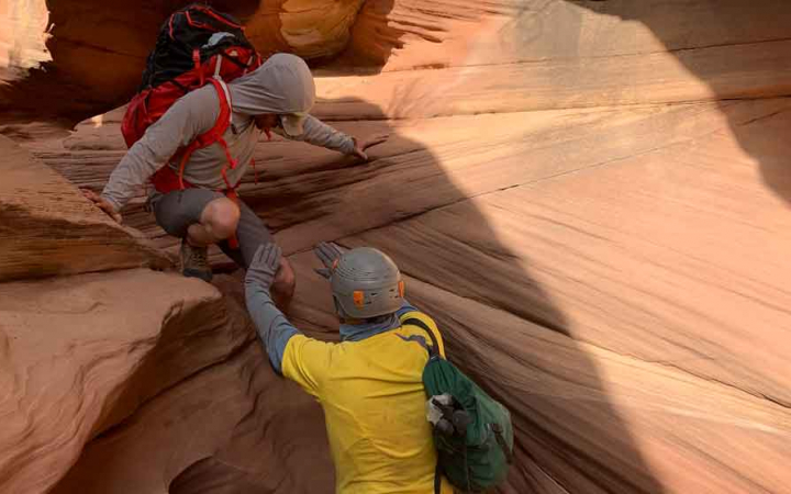 One person helps another navigate a short drop into a canyon.